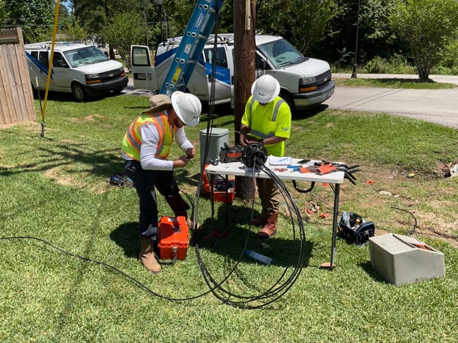 Two technicians splicing at a field table beside a utility pole